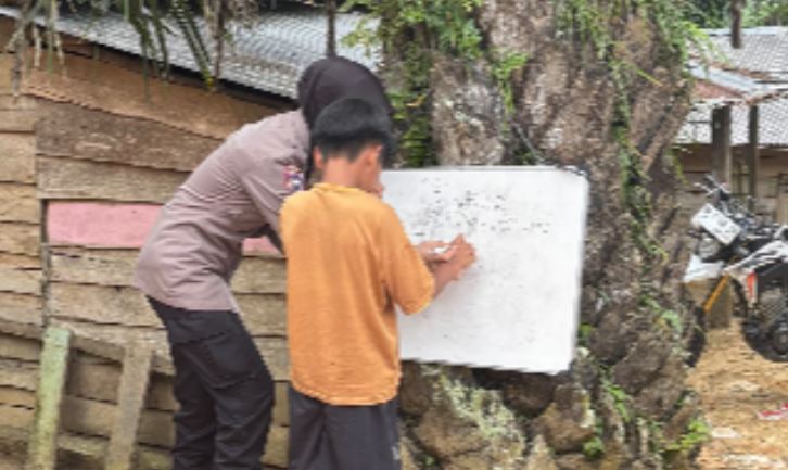 Bripda Nia Kurnia membimbing seorang anak SAD belajar menulis di papan tulis portabel yang dipasang di batang pohon, Desa Bungku, Kecamatan Bajubang, Batanghari, Jambi. Dok. Humas Polsek Bajubang)