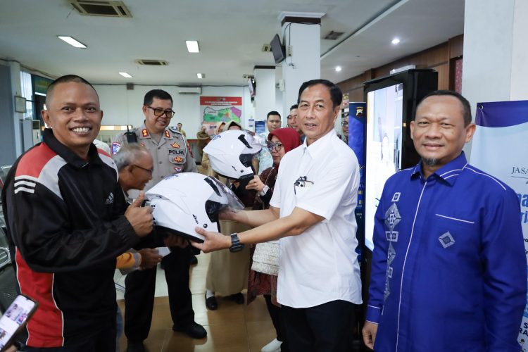Komisaris Jasa Raharja M. Khoerur Roziqin menyerahkan helm kepada wajib pajak tertib sebagai simbol kampanye keselamatan berkendara saat kunjungan kerja di Samsat Kota Semarang III, Senin (29/9/2025). (Dok. Humas JR)