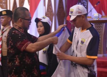 Sekretaris Daerah Provinsi Jambi Sudirman menyematkan atribut kepada salah satu atlet kontingen Jambi saat pelepasan peserta Pekan Olahraga Pelajar Nasional (POPNAS) XVII Tahun 2025 di Auditorium Rumah Dinas Gubernur Jambi, Kamis (30/10/2025). (Dok, Daus)