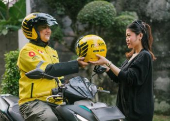 Seorang pengemudi Maxim menyerahkan helm kepada penumpang sebelum memulai perjalanan. Layanan transportasi daring Maxim kini resmi beroperasi di Danau Kerinci dan Bangko, Jambi. (Dok. MAXIM)